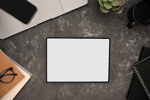 Una maqueta de tableta digital y accesorios de oficina sobre fondo gris cemento grunge