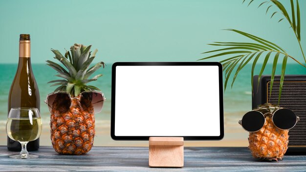 Maqueta de tableta digital y bebidas de verano en una mesa de madera con playa tropical de fondo Concepto de vacaciones de verano