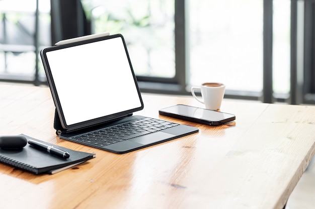 Maqueta de tableta de pantalla blanca en blanco con teclado mágico y gadget en la mesa de madera en la sala de café.