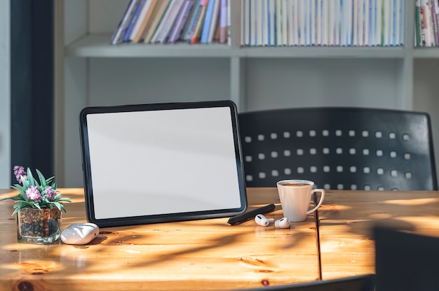 Maqueta de tableta de pantalla en blanco y gadget en la mesa de madera en la sala de estar con luz solar por la mañana.