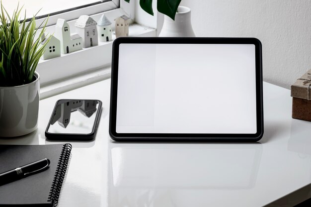 Maqueta de tableta de pantalla en blanco, smartphone y portátil en mesa blanca.