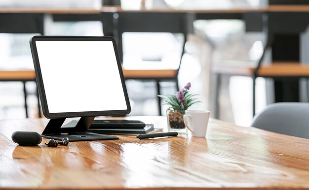 Maqueta de tableta de pantalla en blanco en soporte y gadget en mesa de madera en co-espacio de trabajo.