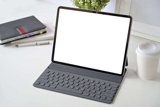 Maqueta de la tableta de la pantalla en blanco con teclado inteligente en la mesa de espacio de trabajo.