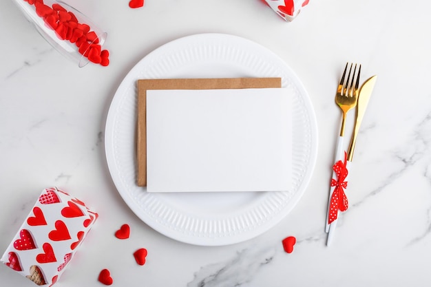 Maqueta de tarjeta del día de san valentín x en plato blanco sobre fondo de mármol con regalo de copa de vino de corazones rojos