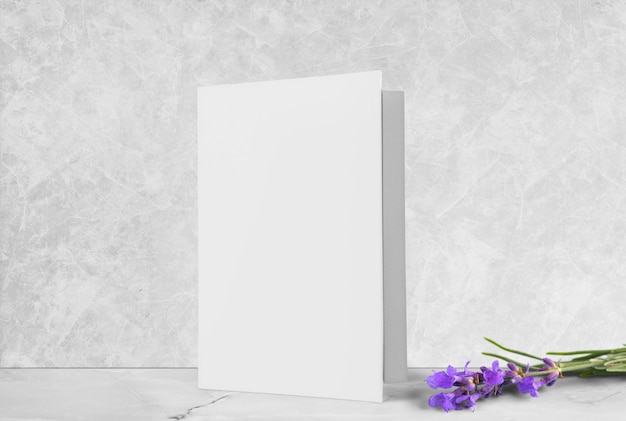 Una maqueta de tarjeta de felicitación blanca, de pie sobre un escritorio de madera blanco con flores