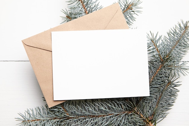 Maqueta de tarjeta de felicitación de Navidad con sobre de papel artesanal y rama de abeto verde fresco sobre fondo de madera blanca vista superior endecha plana Tarjeta de vacaciones de invierno vacía