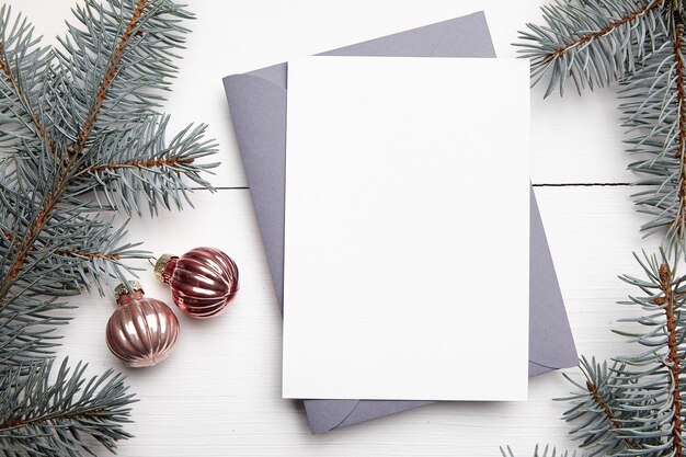 Maqueta de tarjeta de felicitación de navidad con sobre ramas de abeto verde y bolas sobre fondo blanco de madera vista superior plana Maqueta de tarjeta de vacaciones de invierno con decoraciones