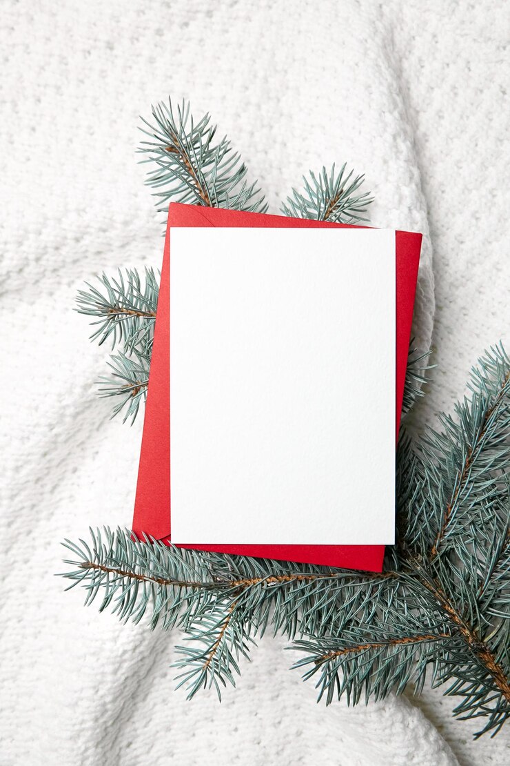 Maqueta de tarjeta de felicitación de navidad con sobre rojo y ramas de abeto sobre fondo de ropa de punto blanco vista superior plana