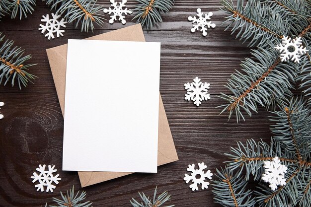 Foto maqueta de tarjeta de felicitación navideña con ramas de abeto verde sobre y copos de nieve blancos sobre marrón