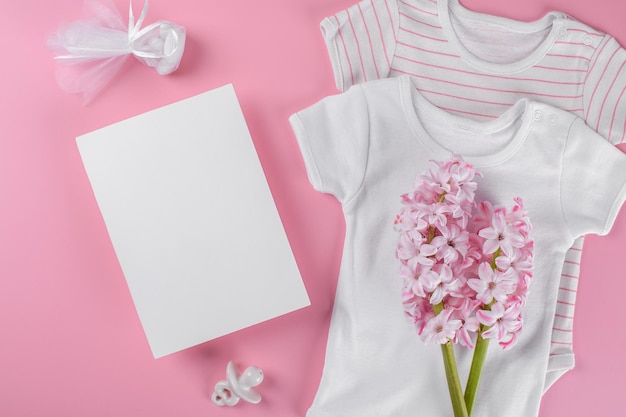 Maqueta de tarjeta de invitación de baby shower 5x7 con accesorios de bebé pezón de mono de niña o caja de regalo ficticia de bebé y confeti y flores de jacinto rosa con espacio de copia sobre fondo de color rosa pastel