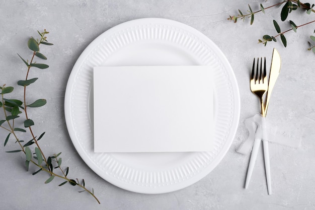 Maqueta de tarjeta de invitación de boda 7x5 en plato blanco sobre fondo gris con mesa festiva de tarjeta de menú de eucalipto