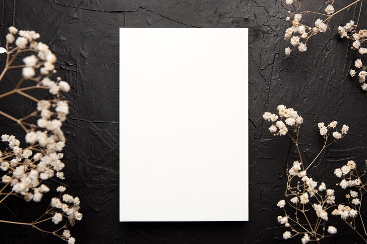 Maqueta de tarjeta invitación de boda en blanco con decoración floral blanca sobre fondo negro Maqueta de tarjeta de felicitación con flores secas en la mesa