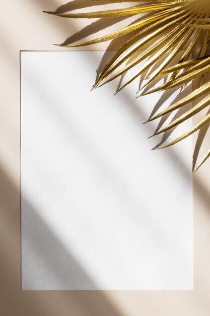 Maqueta de tarjeta de invitación con hojas de palma doradas sobre fondo beige pastel Vista superior espacio de copia plana Plantilla en blanco de maqueta de papel blanco para marca y publicidad