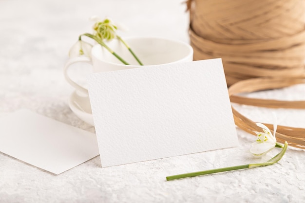 Maqueta de tarjeta de invitación de papel blanco con flores de campanilla de galanthus sobre fondo de hormigón gris espacio de copia de vista lateral