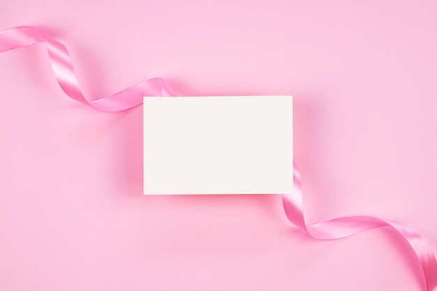 Foto maqueta de tarjeta de papel en blanco sobre fondo rosa con cinta rosa