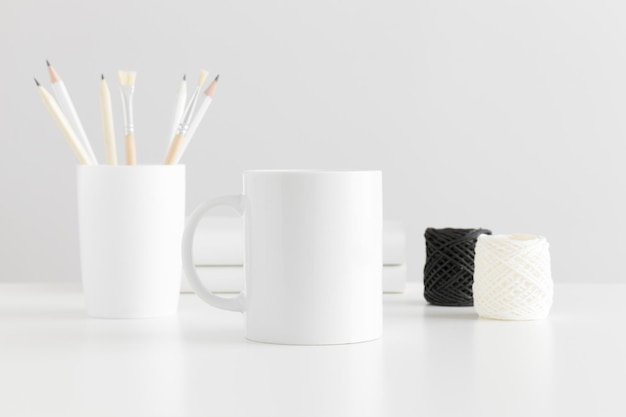 Maqueta de taza con accesorios de espacio de trabajo en una mesa blanca