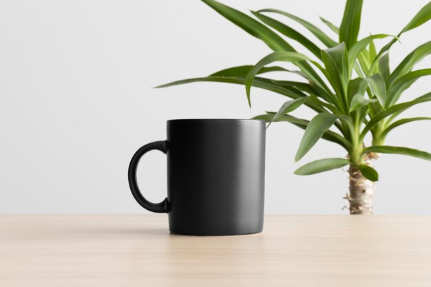 Foto maqueta de taza negra en la mesa de madera con una planta de yuca