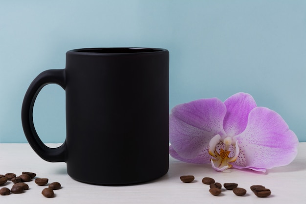 Maqueta de taza negra con orquídeas y granos de café