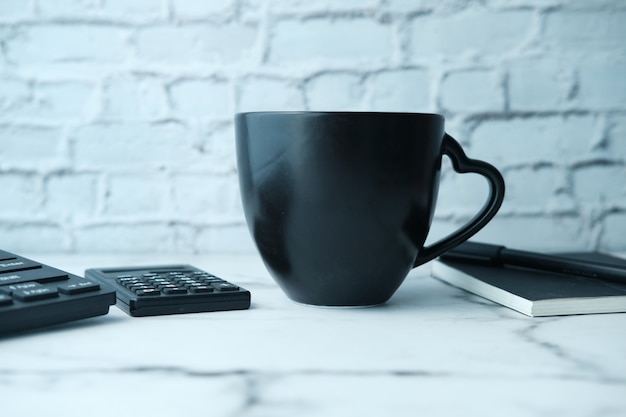 Maqueta de taza negra con teclado, cuadernos en la mesa