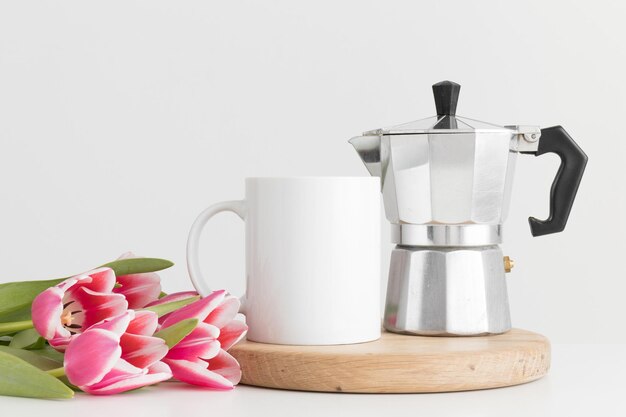 Foto maqueta de taza con un ramo de tulipanes rosas y una cafetera moka sobre una mesa blanca