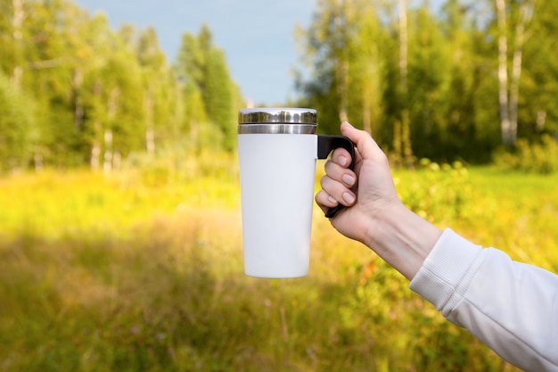 Maqueta de una taza de viaje blanca junto a un abedul. Taza vacía maqueta para promoción de diseño.