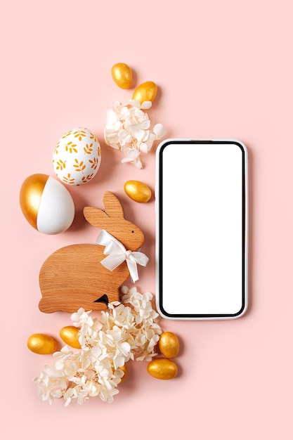 Foto maqueta de teléfono inteligente con dulces de huevos de oro de pascua y flores sobre fondo rosa pastel concepto de vacaciones felices pascuas