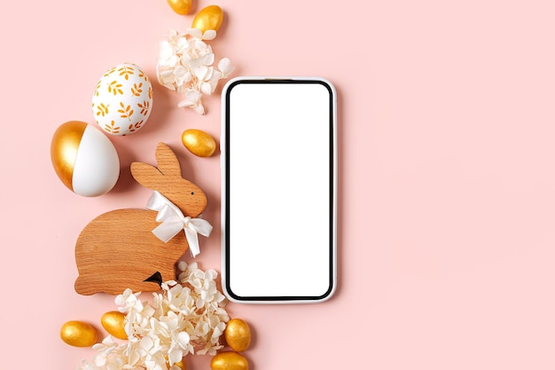 Maqueta de teléfono inteligente con dulces de huevos de oro de Pascua y flores sobre fondo rosa pastel Concepto de vacaciones Felices Pascuas