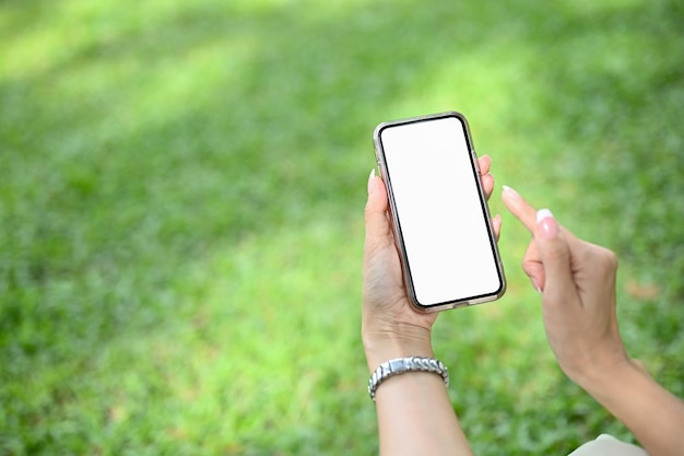 Una maqueta de teléfono inteligente está en la mano de una mujer sobre un fondo de hierba verde borroso