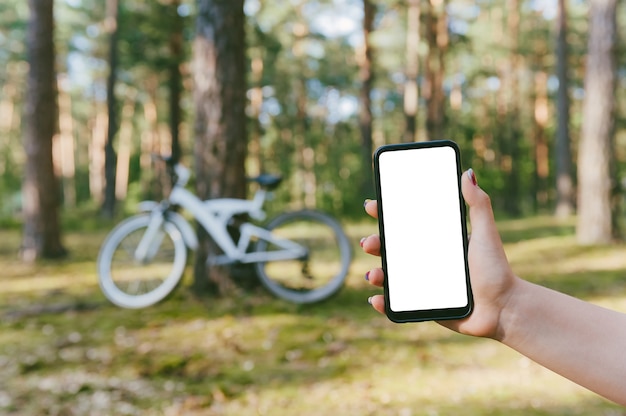 Maqueta de un teléfono inteligente en la mano de una niña. En el contexto de una bicicleta en el bosque.