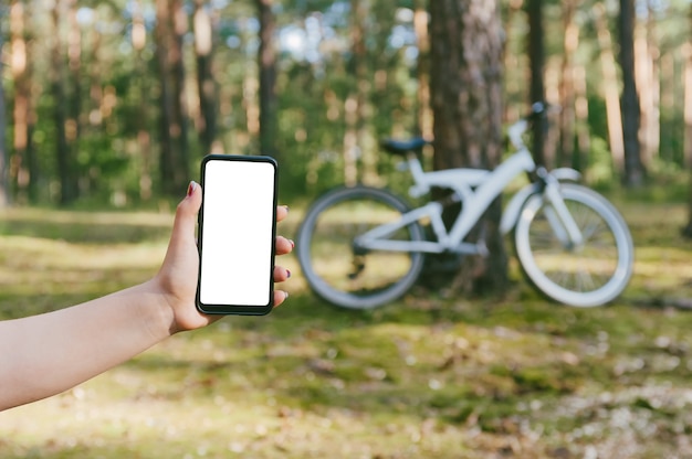 Maqueta de teléfono en la mano de la niña. En el contexto de la naturaleza en bicicleta y bosque.