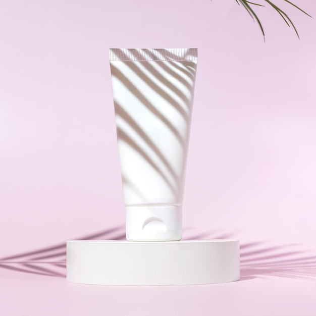 Maqueta de tubo de plástico de botella exprimible blanca para la marca de medicamentos o cosméticos crema gel cuidado de la piel Envase de botella cosmética sobre un fondo rosa en un poduim de hormigón con sombra de hoja de palma