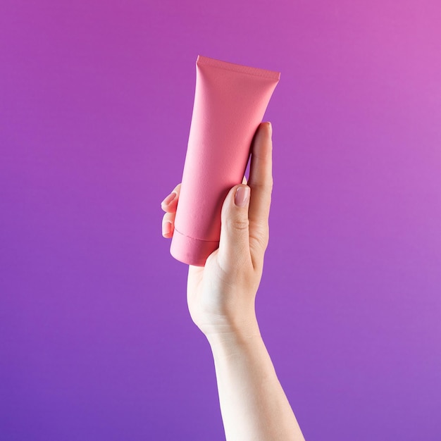 Maqueta de un tubo rosa con un producto cosmético en una mano femenina sobre un fondo morado Espacio de copia Banner