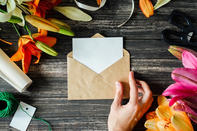 Maquete branco cartão e ofício envelope com flores de lírios em fundo escuro de madeira