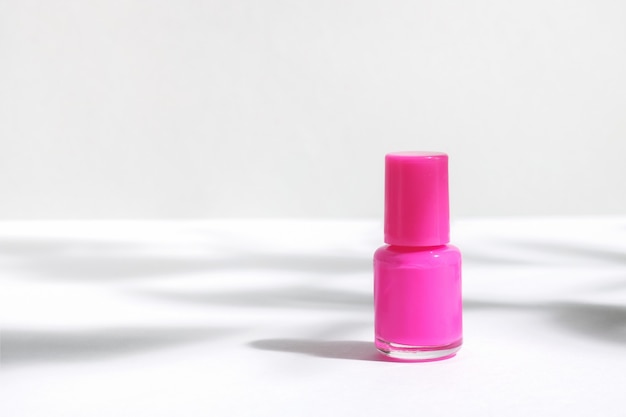Maquete criativa do frasco cosmético isolado com esmalte rosa, sobre fundo branco, com sombras duras de plantas.