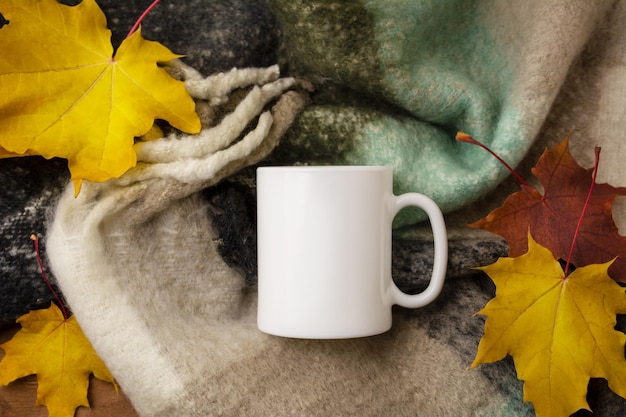 Maquete da caneca de café branco com lenço de lã aconchegante e folhas de bordo de outono. Caneca vazia simulada para promoção de design, modelo estilizado