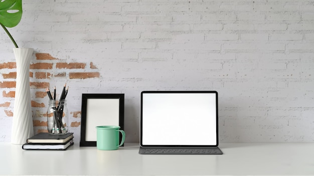 Maquete da tela em branco tablet na mesa de madeira branca e suprimentos