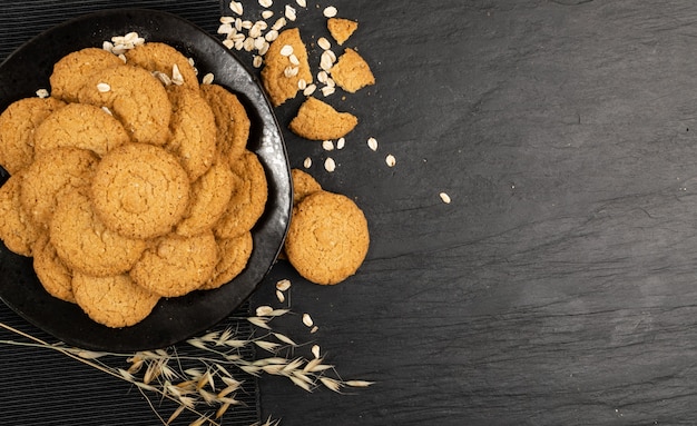 Maquete de biscoitos de aveia finos. Vista superior de biscoitos de aveia de cereais saudáveis em fundo preto. Cookie crocante de biscoito anzac com flocos de aveia com espaço de cópia