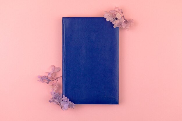 Maquete de bloco de notas de couro azul vazio com composição de borda de flor seca, fundo rosa, foto de vista superior