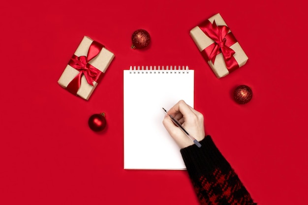 Maquete de caderno Mão com caneta escrevendo em branco caderno vermelho decorações presentes plana leigos em vermelho