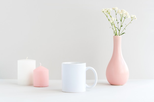 Foto maquete de caneca branca com velas, vaso rosa e galho de gipsófila em uma mesa