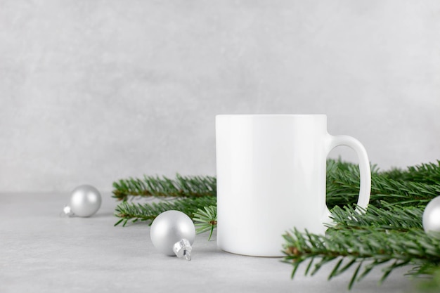 Maquete de caneca branca em branco com galhos de árvores de natal e bolas de prata sobre fundo de pedra de concreto leve Composição de férias Vista lateral Copiar espaço