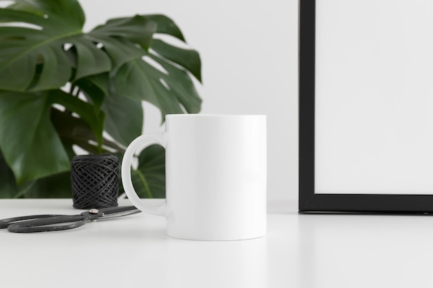 Maquete de caneca com acessórios de espaço de trabalho e uma planta monstera