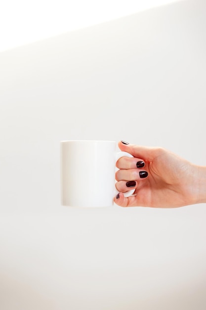 Maquete de caneca de café branco para demonstração de design de copo elegante simulado em mãos femininas em branco