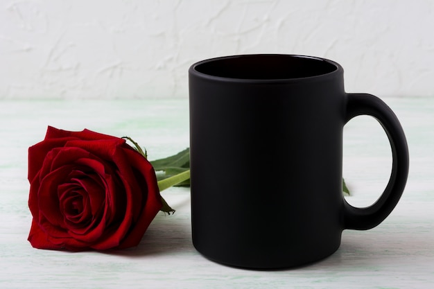 Maquete de caneca de café preto com rosa vermelha