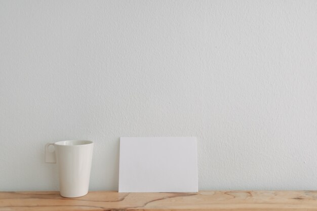 Maquete de cartão branco vazio apoiado em uma xícara de chá com parede branca