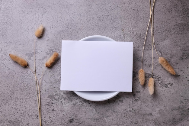 Maquete de cartão de convite branco com flor seca em fundo cinza