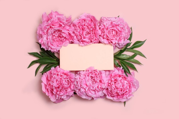Maquete de cartão de convite com papel em branco e delicadas peônias rosa em um fundo rosa pastel