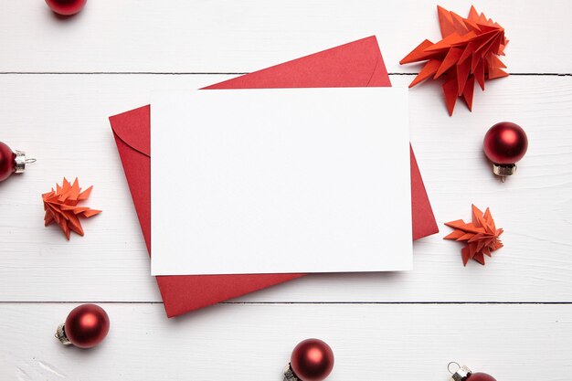 Maquete de cartão de felicitações de Natal com envelope e abetos de papel vermelho em vista superior branca plana
