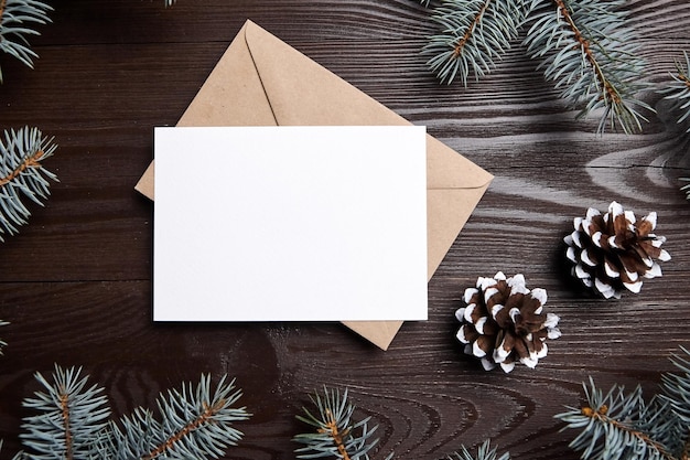 Maquete de cartão de natal com galhos de árvore de abeto verde envelope e cones em fundo de madeira marrom vista superior plana cartão de férias em branco com decoração de inverno