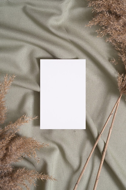 Maquete de cartão de papel branco em branco com grama seca de pampa em tecido de cor neutra verde